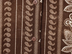Detailed macro view of dark brown paisley print fabric with matching refined buttons