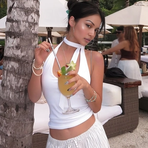 Close-up of white halter neck slim fit top styled with striped pants in a resort setting