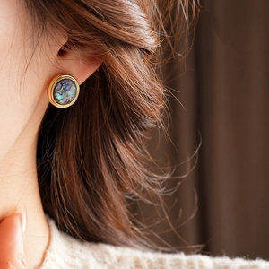 Detailed view of round gold-plated stud earring with blue-green abalone shell inlay