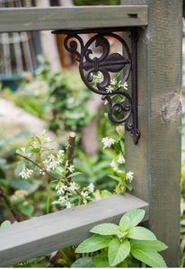 Close-up of a vintage black cast iron bracket with fleur-de-lis design in a garden
