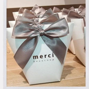 White gift box with grey satin bow and Merci Beaucoup text on wood background