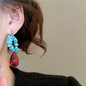 Close-up of bohemian earrings with turquoise stones and red teardrop crystal on model
