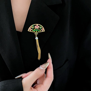 Detailed close-up of fan brooch with gold tassels and pearls on a black suit lapel