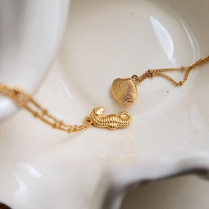Macro view of gold seahorse and shell pendants on a beaded chain necklace