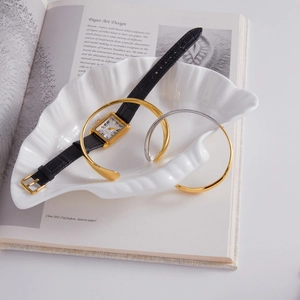 Detailed view of luxury gold bangle and leather watch displayed on paper art book