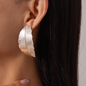 Close-up of metallic feather earrings showing detailed textures and elegant earlobe fit