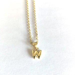 Macro shot of minimalist gold necklace featuring a letter W pendant on white texture