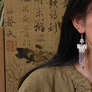 Close-up of butterfly tassel earrings worn by a model against a bamboo scroll