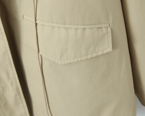 Detailed macro view of khaki trench coat featuring a large flap pocket and drawstring texture
