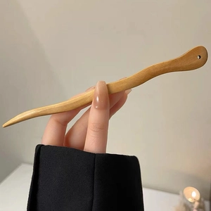 Vue détaillée d'une épingle à cheveux en bois ondulé tenue à la main avec grain naturel