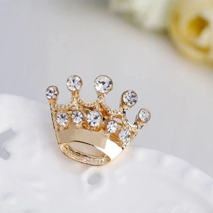 Close-up of a gold hollow crown brooch with sparkling rhinestones on white texture