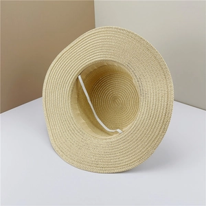 Détail d'un chapeau de paille beige avec mentonnière élastique sur fond épuré