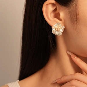 Close-up of model wearing elegant pearlescent flower stud earrings with gold details