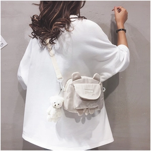 Detail of cute beige canvas crossbody bag with 3D bear ears and plush white charm pendant