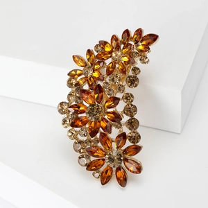 Vintage floral crystal brooch with amber rhinestones on gold base against white background