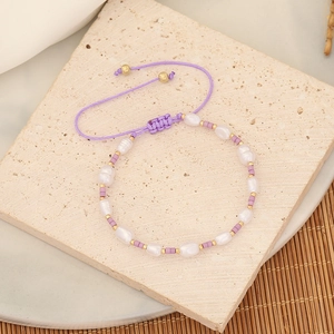Close-up of purple woven beaded bracelet with pearls and gold accents on stone