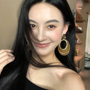 Woven texture gold oval hoop earrings worn by a model in a stylish cafe setting