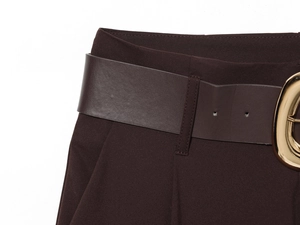 Detail of high-waist brown trousers with matching leather belt and gold oval buckle