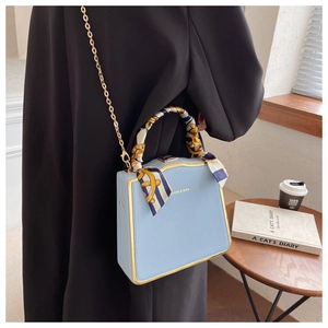 Detail of light blue mini box bag with gold metal frame and silk scarf on the handle
