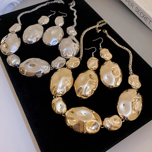 Detailed view of gold and silver irregular oval necklace and earring sets on velvet