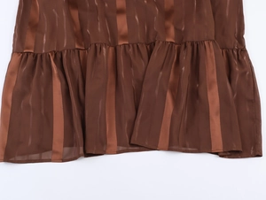 Détail du tissu à rayures marron avec des textures satinées et un ourlet à volants