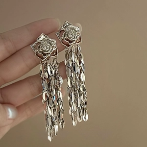 Détail de boucles d'oreilles rose argentée avec glands en écailles tenus à la main sur beige