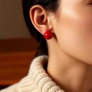Close-up of a model wearing vibrant red spherical stud earrings with a glossy ceramic finish