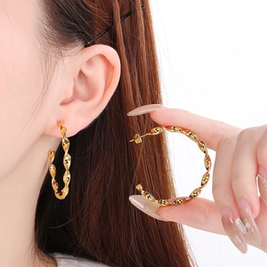 Minimalist twisted gold hoop earrings shown worn on ear and held by model for display