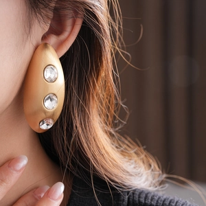Close-up of matte gold oval earrings with three clear crystals worn by a fashion model