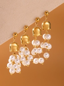Dettaglio macro di orecchini a mughetto con perle bianche e nappa dorata su sfondo beige