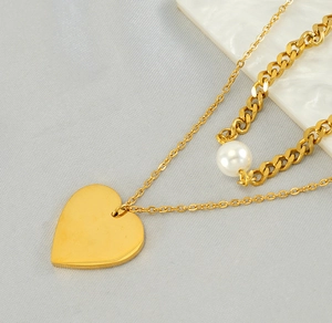 Macro view of double-layered gold heart necklace featuring a large white pearl detail