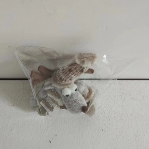 Detail of knitted reindeer plush ornament with scarf and hat in clear packaging
