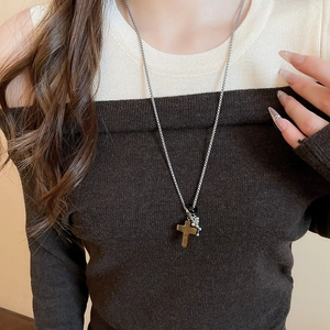 Close-up of a silver beaded necklace with stone cross pendant on a model wearing knitwear