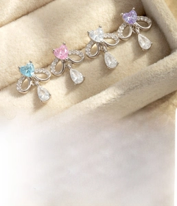 Détail de boucles d'oreilles nœud en acier titane avec zircons cœur bleus et roses