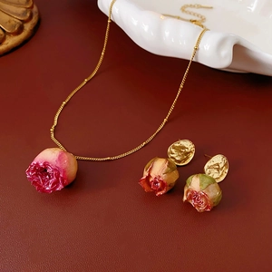 Macro shot of dried rose bud necklace and earrings set on red leather background