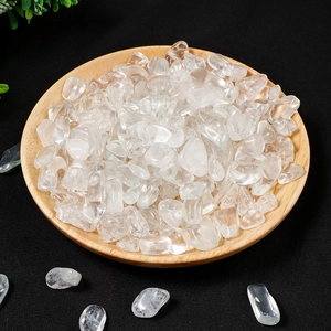 Polished clear quartz tumbled stones in a round wooden bowl on a dark background