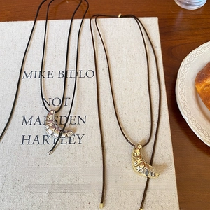 Detailed view of croissant-shaped gold and silver pendants on minimalist black leather cords