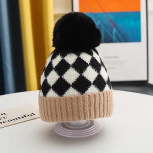 Close-up of baby winter knit hat with checkered pattern and black fluffy pompom detail
