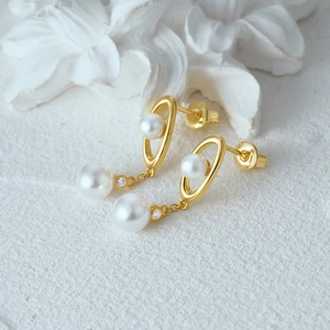 Detailed view of s925 silver gold pearl earrings with zircon on a textured white background