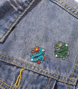 Detailed view of blue and green enamel dragon pins on a denim jacket pocket