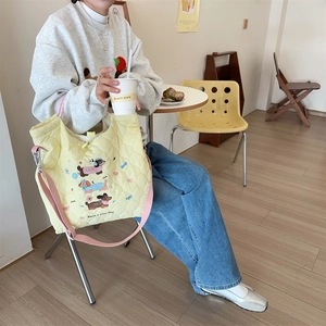 Detail of yellow quilted tote bag with dog embroidery and pink strap in a cafe setting