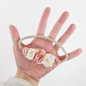 Hand holding beige elastic baby headband with pink and white fabric flowers