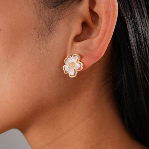 Close-up of white flower stud earring with gold edges and pearl-like finish on model's ear