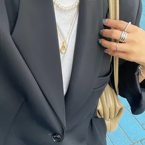 Detail of layered gold heart pendant, pearl necklace, and silver rings on black blazer