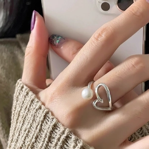 Silver open heart ring with pearl detail worn on finger by a model in soft light