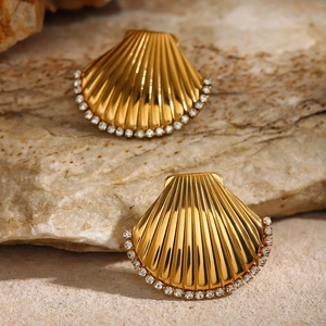 Detailed close-up of golden shell earrings with white rhinestones on natural stone