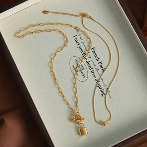 Golden double layer necklace featuring padlock pendant and gold beads on vintage tray