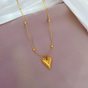Detailed macro view of a gold heart pendant on a beaded chain with a luxury metallic finish