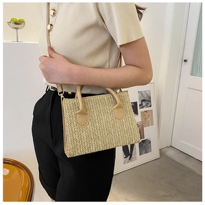 Detail of woven beige straw bag featuring gold hardware and smooth synthetic leather strap