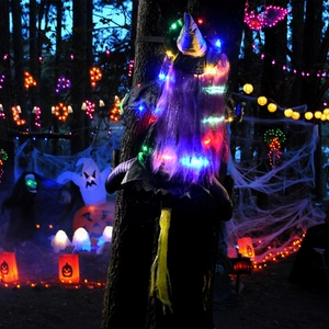 Climbing witch Halloween decoration with purple hair and glowing LED lights on a tree